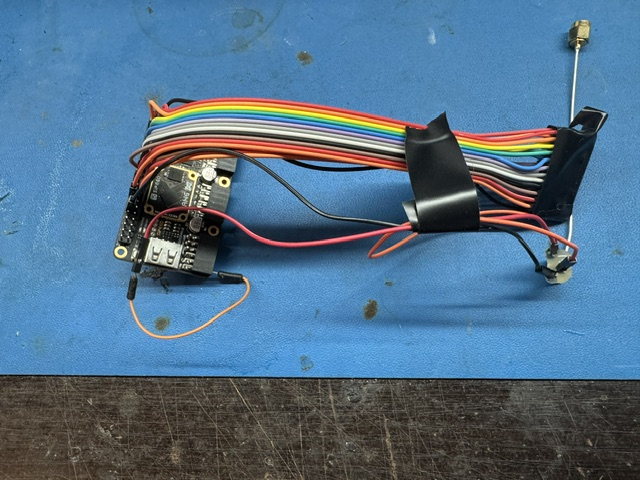 Bench setup for the diversity GNSS antenna work: the FPGA board, a taped ribbon harness and a whip antenna on a stand.